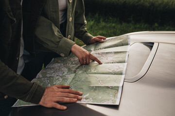 Man and Woman Young Travelers Using Map Near Their Car on Road Trip