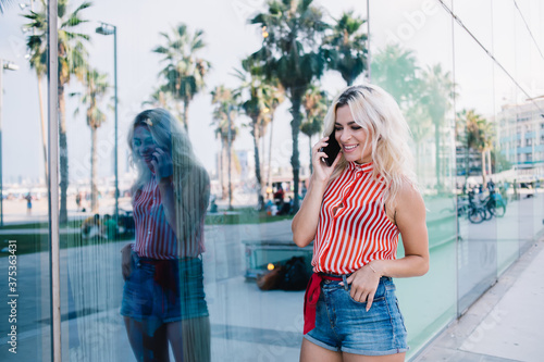 Carefree hipster girl enjoying positive mobile conversation in roaming, happy Caucasian woman in casual apparel connecting to 4g wireless for making friendly smartphone calling at city urbanity
