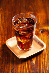 Wall Mural - glass of cold cola soft drink with ice on wooden background