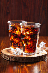 Wall Mural - glass of cold cola soft drink with ice on wooden background