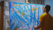 © DC Studio - Guy painting with fingers on large canvas in art studio.