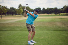 Man Playing Golf Swinging At The Ball As He Plays His Shot Using A Driver Viewed From Behind Looking Down The Fairway In A Healthy Active Lifestyle Concept