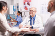 © DC Studio - Senior doctor writing notes on clipboard during examination of young couple with fertility illness in hospital office and nurse holding patient x-ray.