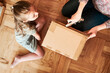 © Przemek Klos - Woman unpacking a cardboard box parcel in room at home. Little girl waiting for opening a gift in package