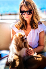 Wall Mural - Attractive woman enjoying summer sunshine while relaxing with her puppy by the sea