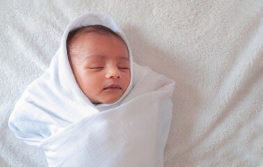 a one month old baby sleeping and swaddled in white cloth lying in white cloth background