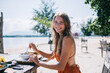 © BullRun - Glad adult woman eating while sitting at table on sea sand shore in fair weather