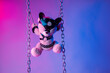 © rotozey - toy bear dressed in leather belts harness accessory for BDSM games on a dark background in neon light