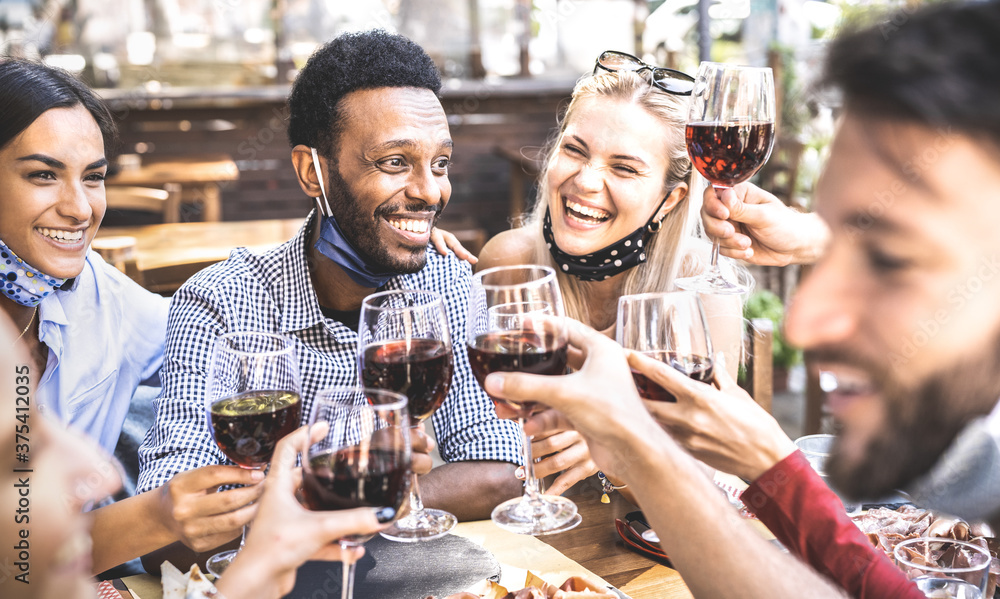 Friends toasting red wine at outdoor restaurant bar with open face mask - New normal lifestyle concept with happy people having fun together on warm filter - Focus on afroamerican guy - obrazy, fototapety, plakaty 