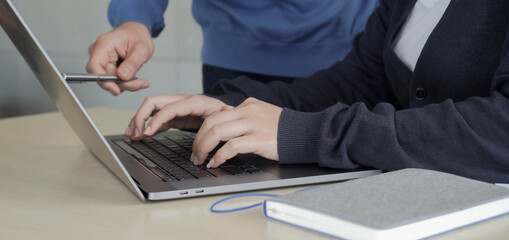 close up on manager man hand using pen to explaining about company's project on laptop screen with employee woman type on keyboard to help and advice about marketing strategy concept