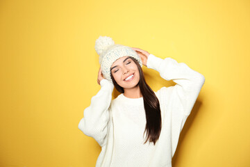 Poster - Happy young woman wearing warm sweater and knitted hat on yellow background