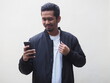 © KrishnaTedjo - An adult Asian man wearing black jacket and white shirt doing proud and happy gesture while looking to mobile phone isolated on white. Space for copy