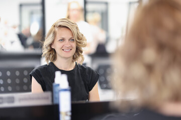 Wall Mural - Woman with an evening hairstyle in a beauty salon sits in front of mirror and smiles. Creating an image for celebrations concept