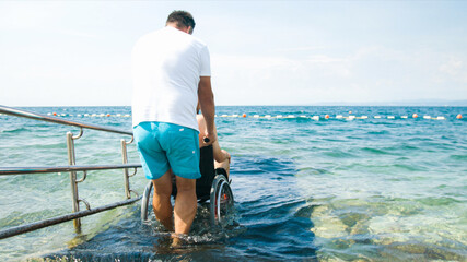 Wall Mural - Disabled man at beach swimming on a wheelchair with assistance help on an accessible ramp.