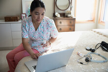 Home Caregiver With Pillbox Using Laptop On Bed