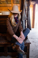 Female Rancher Putting On Cowboy Boots In Barn