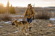 Male Hunter With Dog Walking In Field At Sunset