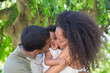 © Tom Merton/Caia Image - Affectionate parents kissing toddler daughter below tree