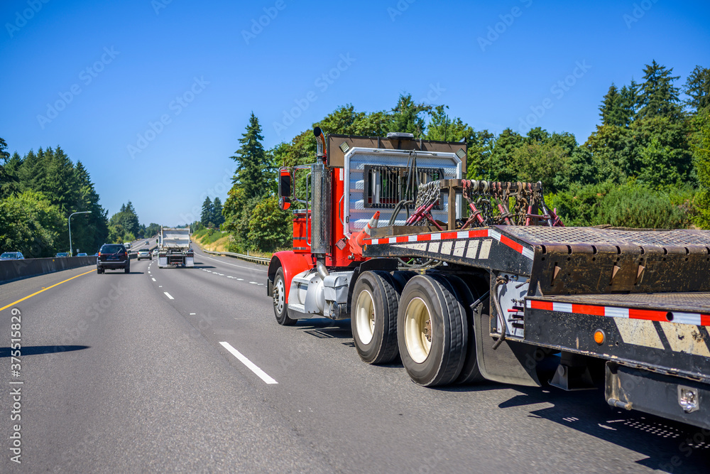 Red bright big rig semi truck with step down semi trailer running on ...