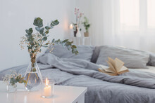 Burning Candles And Eucalyptus In Glass Vase In White Bedroom