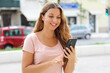 © zigres - Brazilian woman typing on smartphone in city street with traffic cars on background