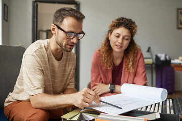 Wall Mural - businessman in eyeglasses sitting at the table pointing at blueprint and discussing it with his coll