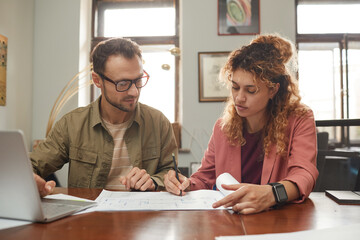 Wall Mural - two designers sitting at the table and working in team they drawing blueprint and planning new proje