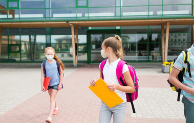 Poster - education, childhood and pandemic concept - group of elementary school students wearing face protective medical mask for protection from virus disease with backpacks walking and talking outdoors