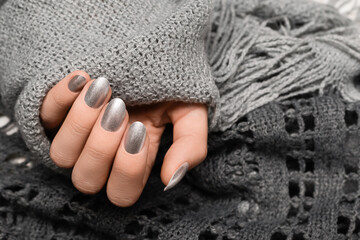 Female hand with silver nail design. Silver nail polish manicured hand. Woman hands hold grey wool shawl.