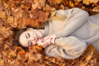 © Kiryl Lis - Happy smiling cute girl with closed eyes liying in the autumn leaves and enjoying it, holding face and smiling. Autumn portrait in the autumn park. Top view.