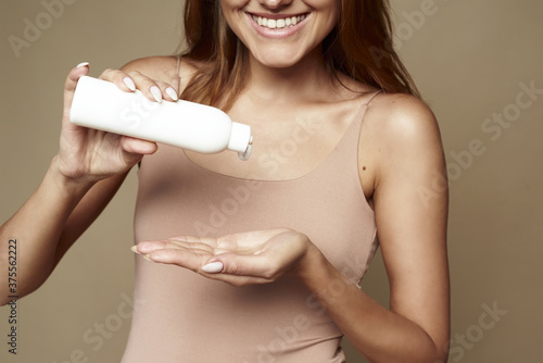 Cuadros en Lienzo Young woman in a beige bodysuit squeezes moisturizer onto her arm in the studio