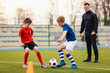© matimix - Young boys on soccer practice training with coach. Junior footballers compete on training unit. Young coach coaching sports school kids. School soccer stadium in blurred background