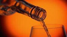 Hard Alcohol Or Wine Pouring Into Glass On Orange Spotted Background. Slow Motion. Wine Pour From Bottle