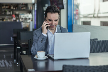 Wall Mural - Positive businessman with laptop talking on phone in cafe