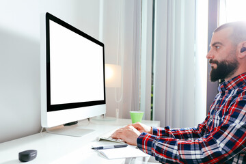 Young man working in front of computer with blank screen at home