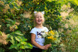 © Svitlana - A charming four-year-old blonde girl with a bouquet of wildflowers laughs loudly. Portrait of a girl outdoors with funny hair ties in the form of rabbits. Children Protection Day. Joy, emotions