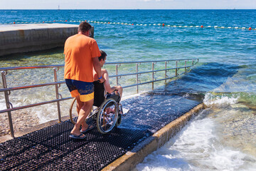 Wall Mural - Man on wheelchair on accessible beach with ramp. Disabled person going for a swim.