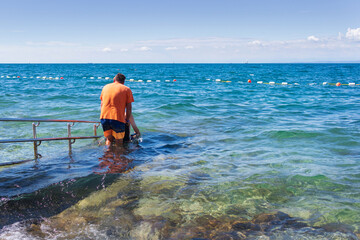 Wall Mural - Man on wheelchair on accessible beach with ramp. Disabled person going for a swim.