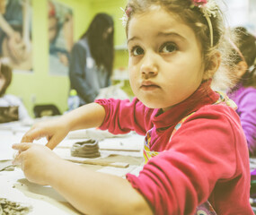 Wall Mural - Portrait of creative little girl working with clay at pottery workshop.