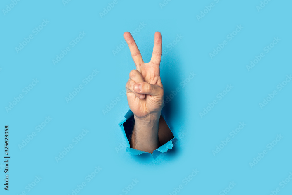 Male hand makes a two fingers up greeting gesture on a blue background. Banner - obrazy, fototapety, plakaty 