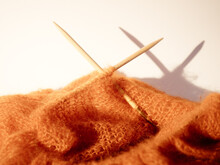 Knitting Needles And Orange Wool On A Creamy White Background