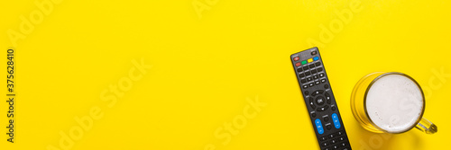 Fotografía Remote control from the TV or TV tuner, a glass of beer on a yellow background