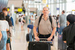 © shine - Handsome senior man with backpack walking with a luggage at airport terminal and airport terminal blurred crowd of travelling people on the background.