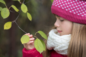 Wall Mural - Pretty child girl wearing warm winter clothes holding tree branch with green leaves in cold weather outdoors.