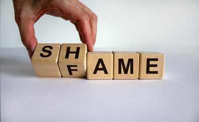 Hand turns cubes and changes the word shame to fame. Beautiful white background. Business concept. Copy space.