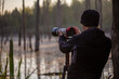 professional photographer shooting wild in early morning at summer swamp area with telephoto lens on a tripod