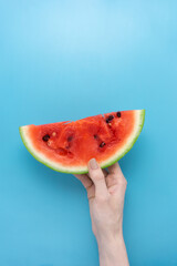 Creative food health diet concept photo of hand holding sliced watermelon fruit on blue background.