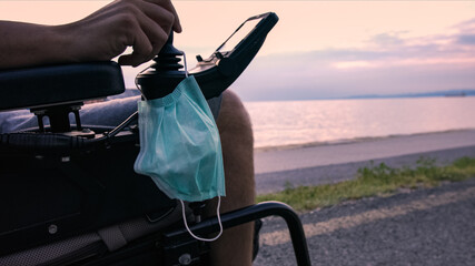 Wall Mural - Face mask on wheelchair near sea at sunset.