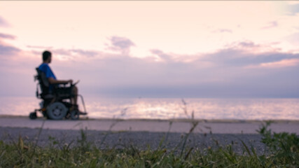 Wall Mural - Man on wheelchair near sea at sunset.