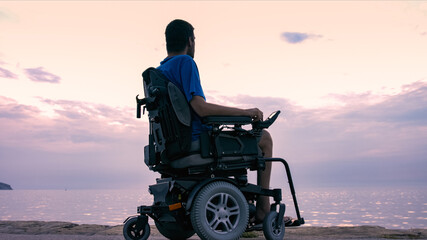 Wall Mural - Man on wheelchair near sea at sunset.